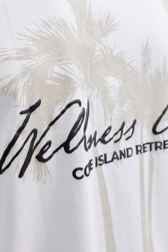 Wit T-shirt met korte mouwen van CORE BY JACK & JONES met een grafische opdruk van lichtgrijze palmbladeren en zwarte, verhoogde letters 'Wellness COE ISLAND RETRE'.
