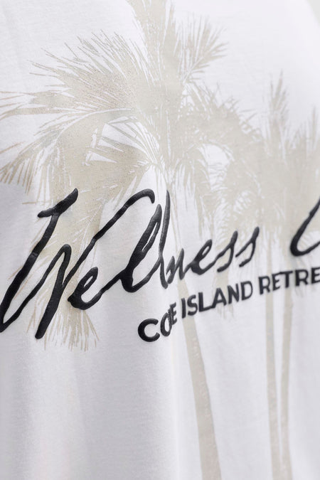T-shirt blanc à manches courtes de CORE BY JACK & JONES avec un imprimé graphique de feuilles de palmier gris clair et les lettres noires en relief 'Wellness COE ISLAND RETRE'.
