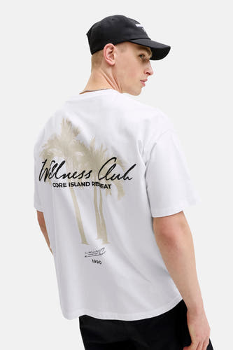 Wit T-shirt met korte mouwen van CORE BY JACK & JONES, met 'Wellness Club CORE ISLAND RETREAT' en palmbomen op de rug, gedragen door een man.