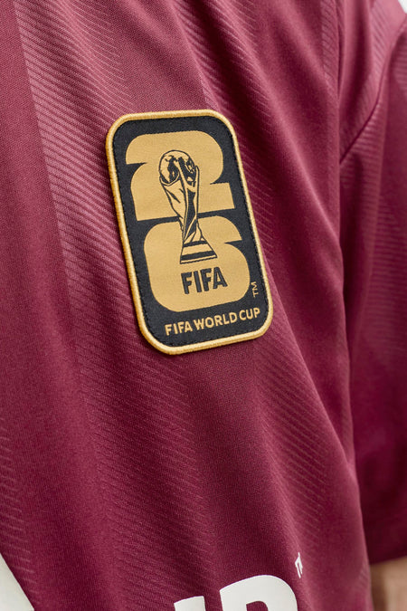 Polo marron de la marque ORIGINALS BY JACK & JONES avec tissu à rayures diagonales et écusson doré de la Coupe du Monde de la FIFA 26.