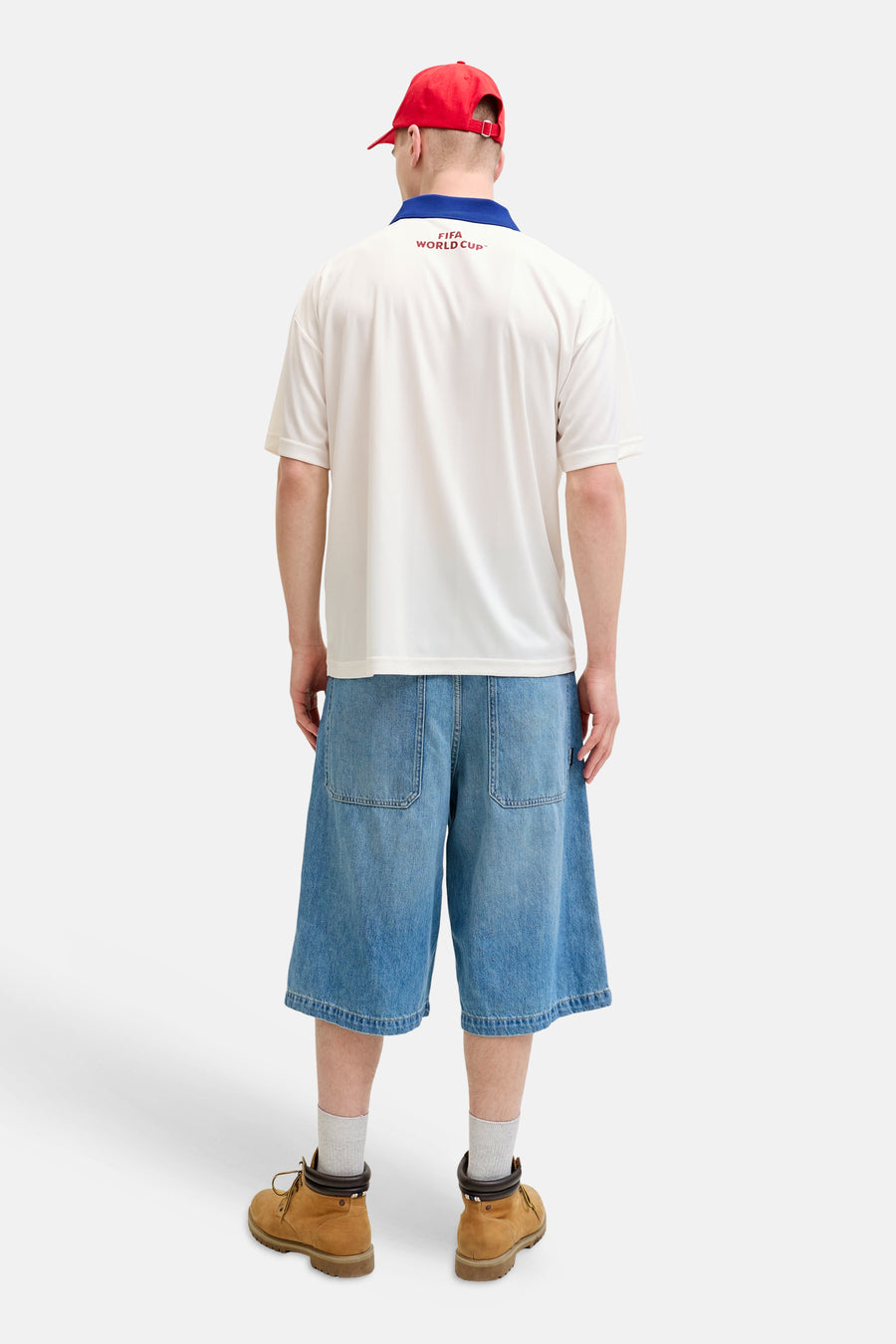 Wit poloshirt van ORIGINALS BY JACK & JONES met blauwe kraag en rode 'FIFA WORLD CUP™' op de rug, gedragen met rode pet en denim shorts.