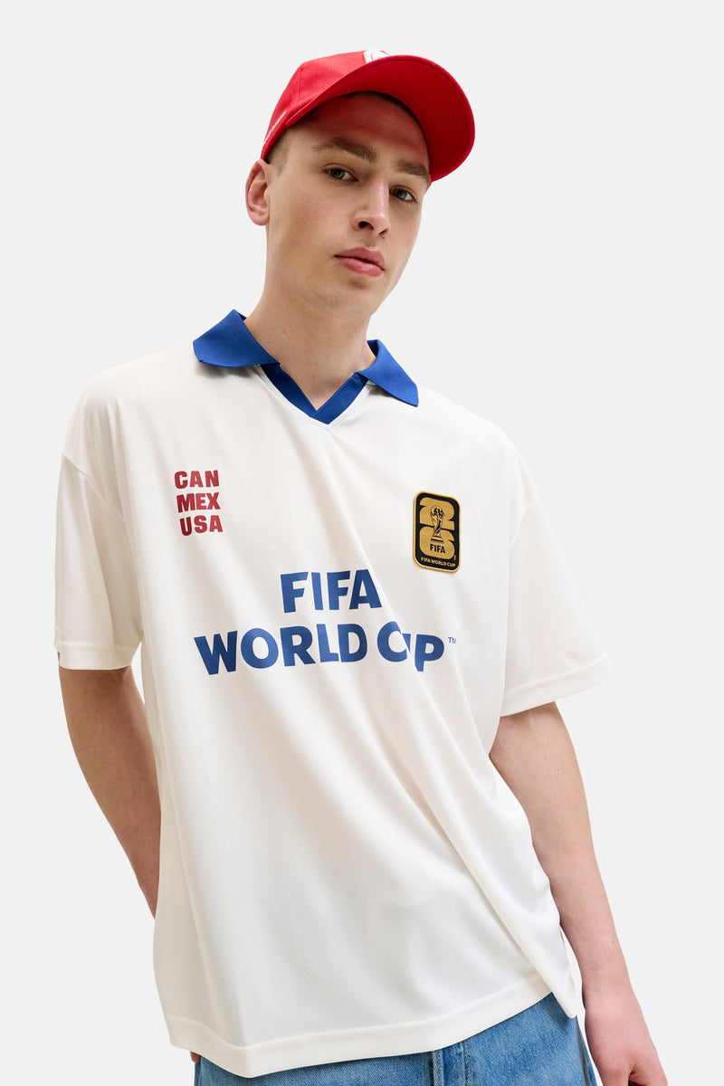 Witte polo van ORIGINALS BY JACK & JONES met blauwe kraag, FIFA World Cup 2026 logo, blauwe 'FIFA World Cup' en rode 'CAN MEX USA' teksten.