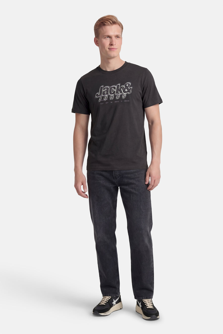 T-shirt gris à manches courtes de CORE BY JACK & JONES, avec un imprimé graphique et combiné avec un jean noir et des baskets.