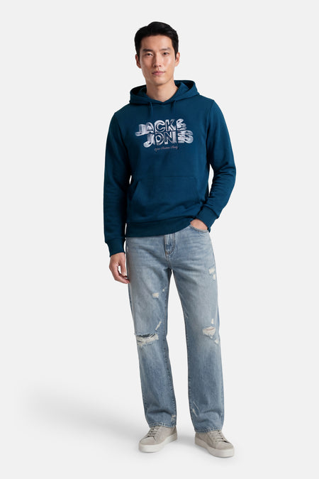 Blauwe sweater met kap van CORE BY JACK & JONES, met print op de borst, gecombineerd met gescheurde jeans en sneakers.