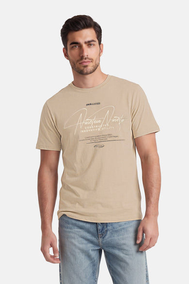 T-shirt beige de CORE BY JACK & JONES avec imprimé graphique blanc, porté par un homme en jean bleu.