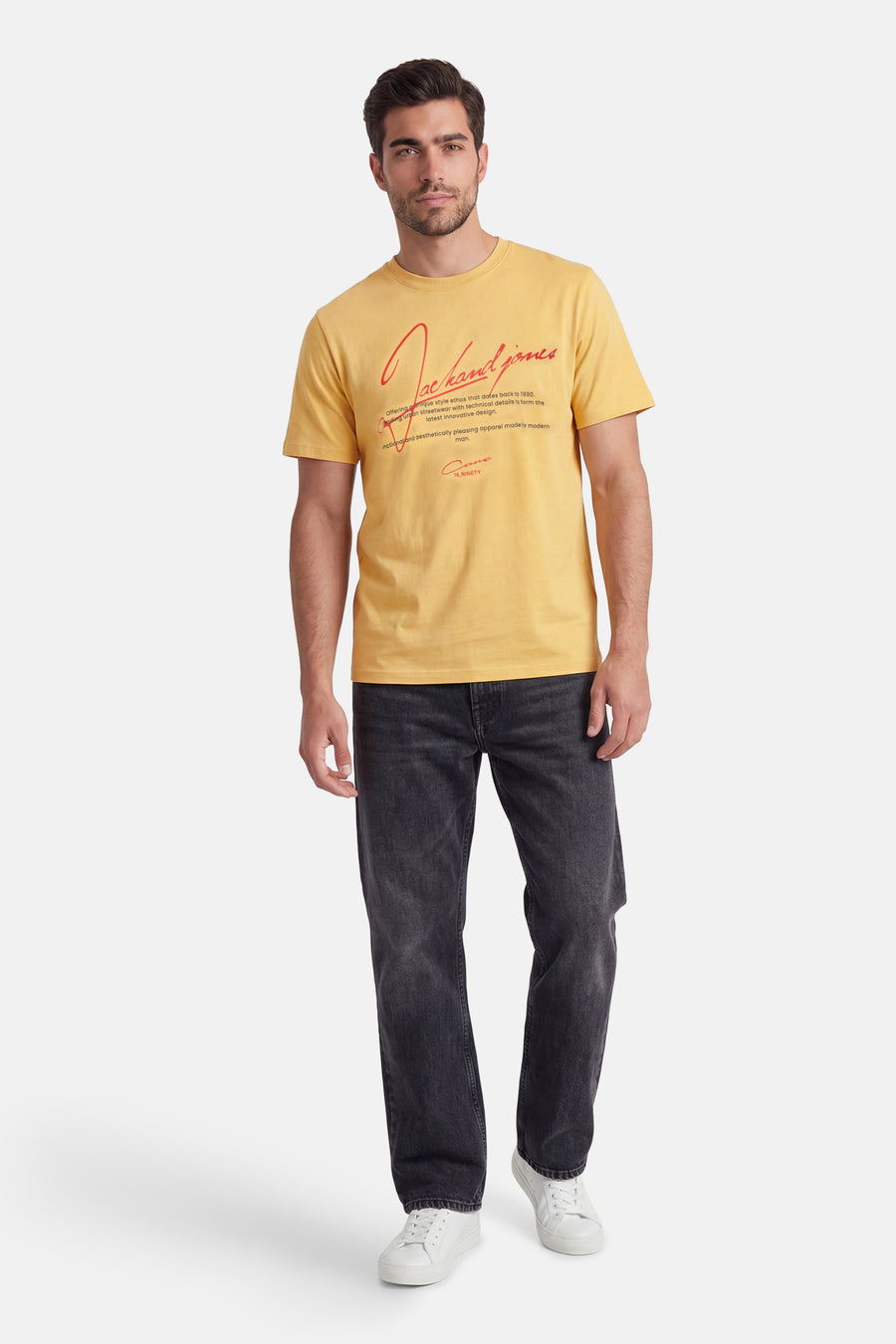 Geel T-shirt met korte mouwen van CORE BY JACK & JONES met rode tekst op de voorkant, gedragen door een model met donkere jeans en witte sneakers.