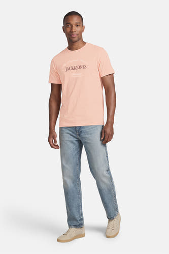 T-shirt rose de Originals by Jack & Jones avec imprimé texte blanc style vintage et col rond, porté avec un jean clair et des baskets beiges.