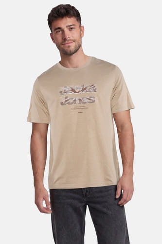 Beige T-shirt van CORE BY JACK & JONES met een getextureerde JACK & JONES-print, gedragen door een man met donkere jeans.