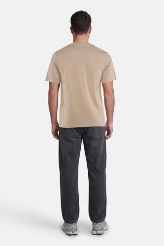 Beige T-shirt van CORE BY JACK & JONES, achterkant van een man die het draagt met donkere jeans en sportschoenen.