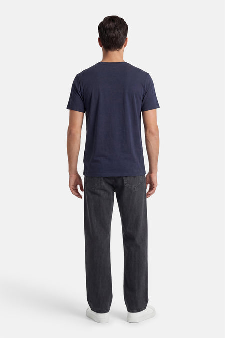 Donkerblauw T-shirt van ORIGINALS BY JACK & JONES, aan de achterkant gedragen door een man met een geribbelde donkergrijze broek en witte sneakers.