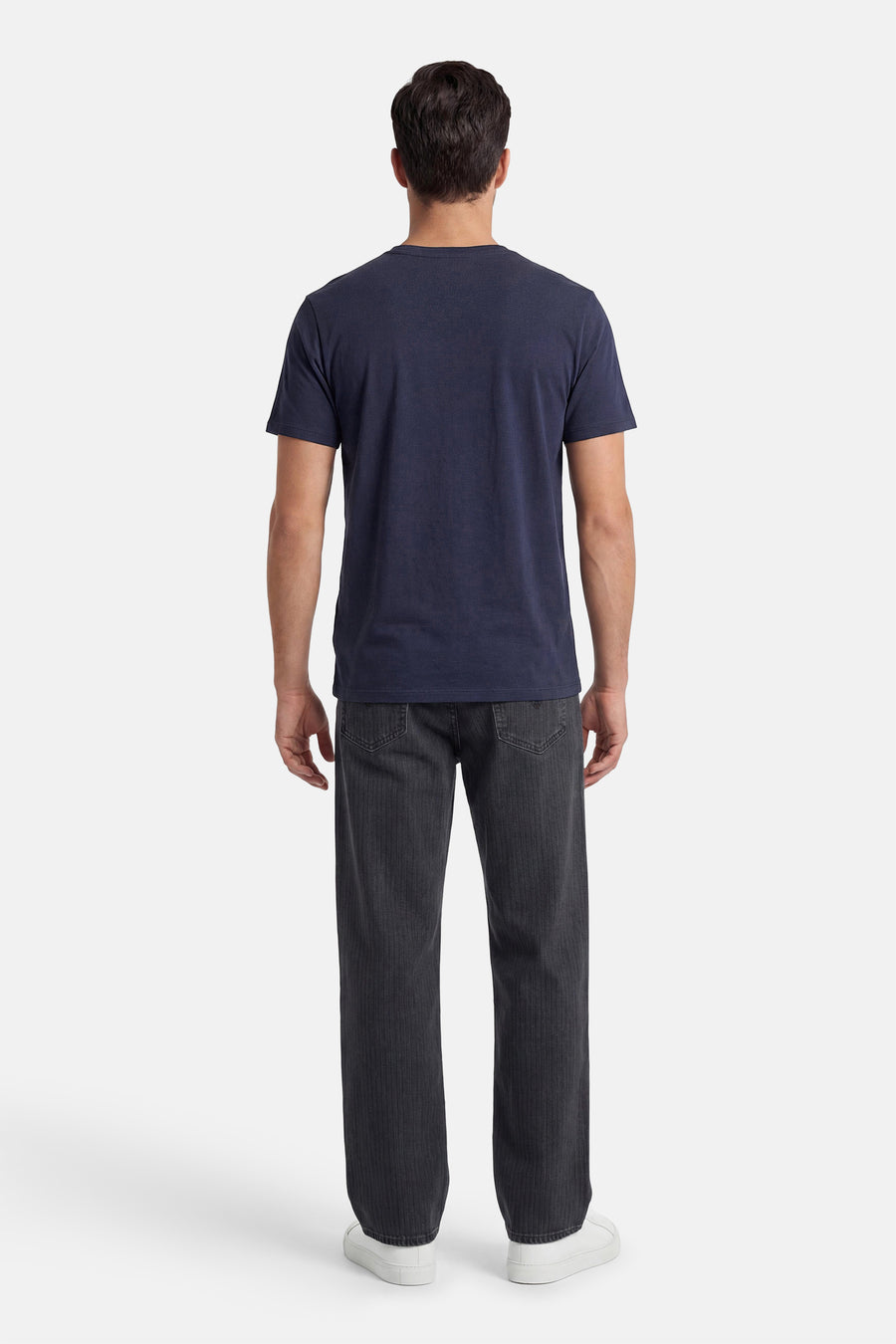 Donkerblauw T-shirt van ORIGINALS BY JACK & JONES, aan de achterkant gedragen door een man met een geribbelde donkergrijze broek en witte sneakers.