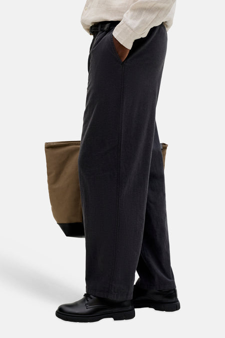 Zwarte seizoensbroek van JACK & JONES JEANS INTELLIGENCE met elastische taille en losse pasvorm, gedragen met een licht overhemd, zwarte schoenen en bruine tas.