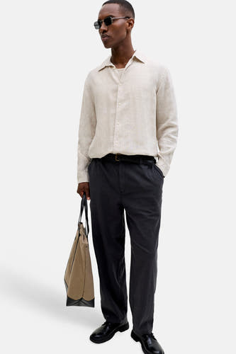Pantalon noir extensible pour homme de JACK & JONES JEANS INTELLIGENCE, porté avec une chemise beige et des chaussures noires.