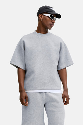 Grijze ronde-hals sweater van CORE BY JACK & JONES, oversize fit, melange stof, model in lifestyle pose met zwarte pet en witte zonnebril