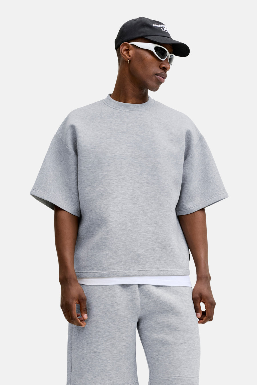 Grijze ronde-hals sweater van CORE BY JACK & JONES, oversize fit, melange stof, model in lifestyle pose met zwarte pet en witte zonnebril
