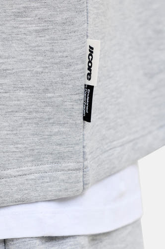 Grijze ronde hals sweater van CORE BY JACK & JONES, met zachte melange stof en witte label, gedragen over een witte t-shirt, close-up detail.