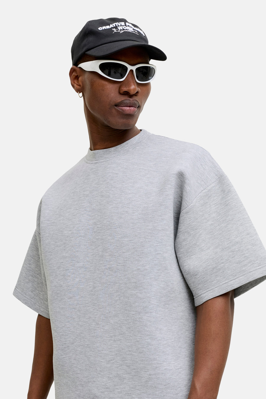 Grijze ronde hals sweater van CORE BY JACK & JONES, met marl textuur, oversized fit, model in lifestyle shot met zwarte pet en witte zonnebril