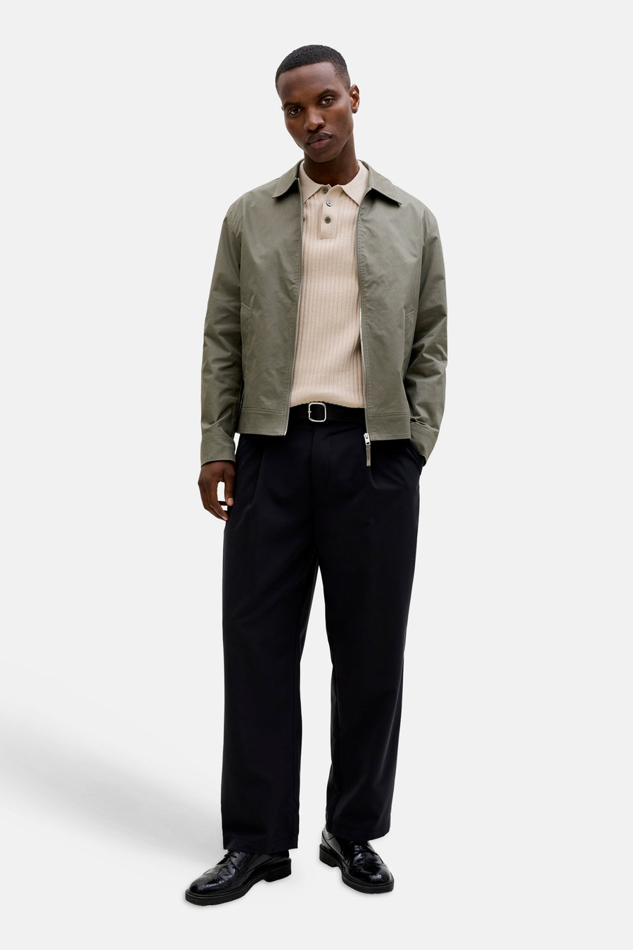 Beige geribbelde poloshirt van PREMIUM by JACK & JONES, gedragen onder een open groen jasje met zwarte broek en lakschoenen.