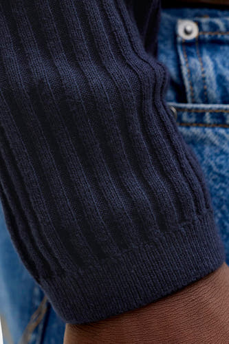 Pull en tricot côtelé bleu foncé de PREMIUM by JACK & JONES, gros plan sur la manche par-dessus un jean et peau visible.