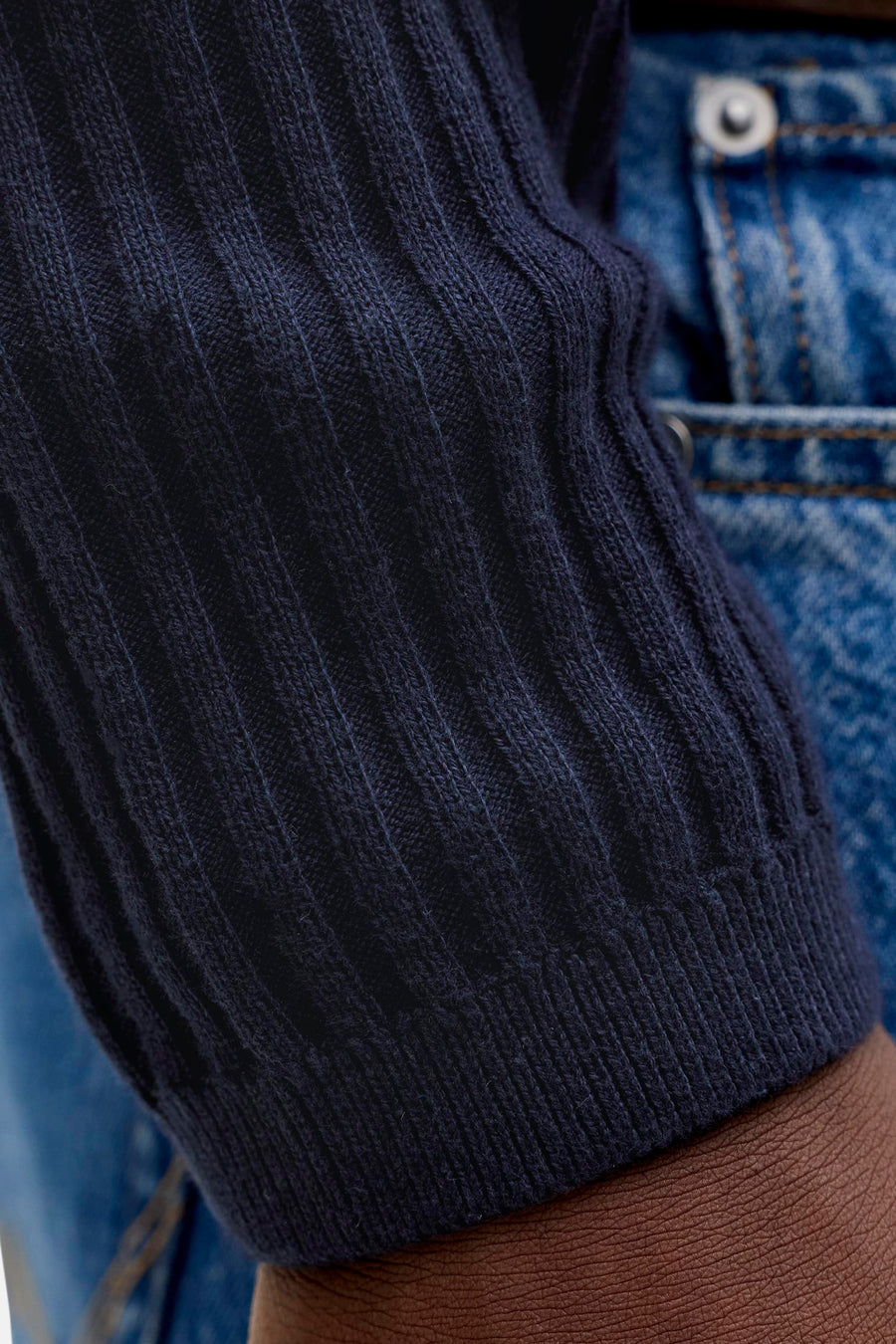 Pull en tricot côtelé bleu foncé de PREMIUM by JACK & JONES, gros plan sur la manche par-dessus un jean et peau visible.