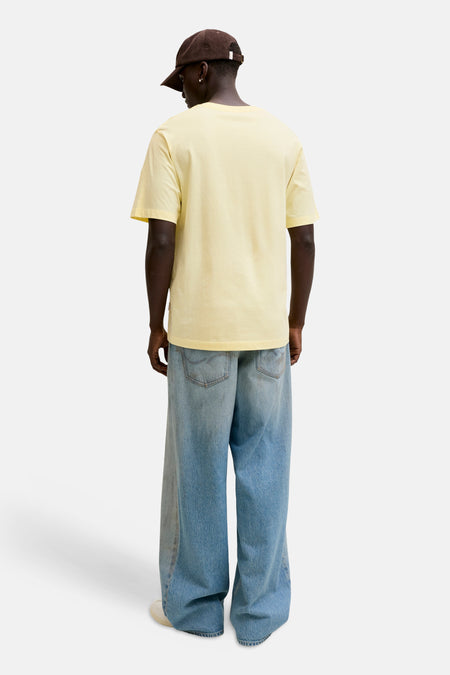 T-shirt jaune à manches courtes de ORIGINALS BY JACK & JONES, vue de dos, porté par un homme avec une casquette marron et un jean ample.