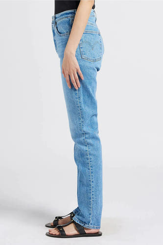 Lichtblauwe straight jeans van Levi's, zijaanzicht met hand op het bovenbeen en zwarte sandalen.

