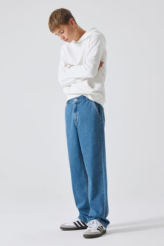 Jean décontracté de denim bleu moyen de LMTD, porté avec une hoodie blanche et des baskets blanches à rayures noires.