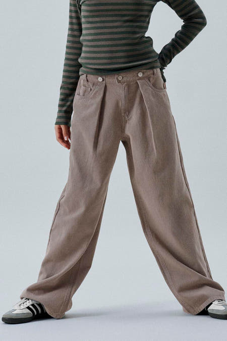 Bruine broek van LMTD, met plooien en wijde pijpen, gecombineerd met een gestreepte top en sneakers.
