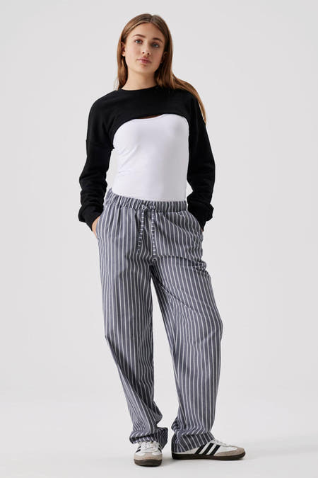 Zwarte denim trui van LMTD, gecombineerd met een witte top en gestreepte grijze broek, met vetersluiting en sneakers.