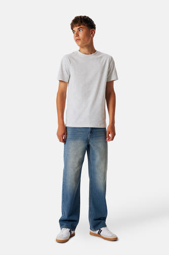 Wijdvallende jeans in middenblauw denim van LMTD, gedragen met een grijs T-shirt en witte sneakers.
