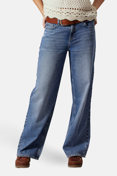 Jean en denim bleu large de LMTD, avec une ceinture marron et des chaussures marrons.