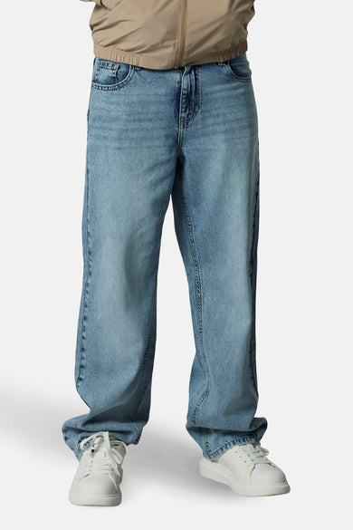 Lichtblauwe denim jeans wide van LMTD, met witte sneakers en een beige jas.
