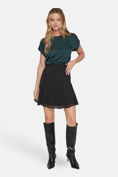 Groene T-shirt van VILA, met korte mouwen, gecombineerd met een zwarte rok en zwarte laarzen.
