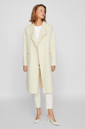 Ecru jas van VILA, met open voorkant, steekzakken en gedragen met witte top, broek en pumps.
