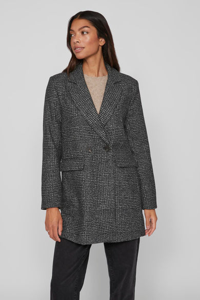 Manteau court noir de VILA, avec une impression en tweed gris, associé à des jeans noirs et des bottes en cuir.