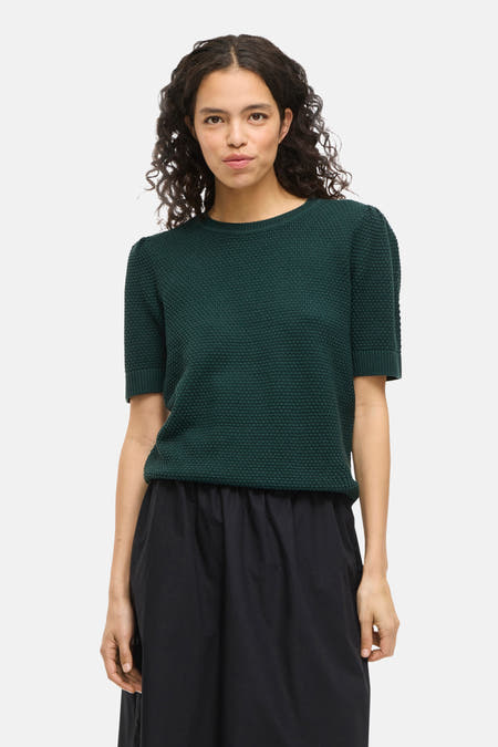 Groene trui van VILA®, met korte mouwen en een subtiele textuur, gecombineerd met een zwarte rok.
