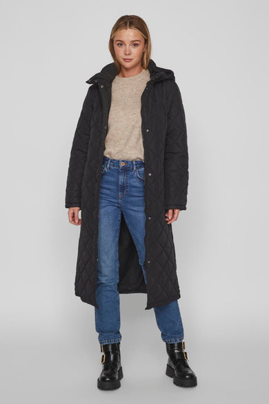 Manteau long noir de VILA avec motif à carreaux, capuche, porté sur une chemise beige et des jeans bleus avec des bottes noires.