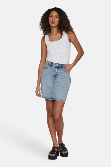 Korte rok van lichtblauwe denim van VILA, met een witte tanktop en zwarte sandalen met plateauzolen.
