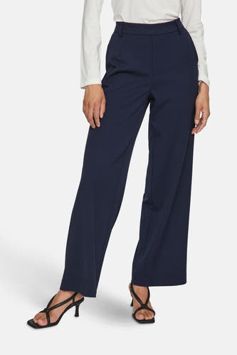 Pantalon bleu de VILA, avec des jambes larges, associé à un chemisier blanc et des baskets noires.