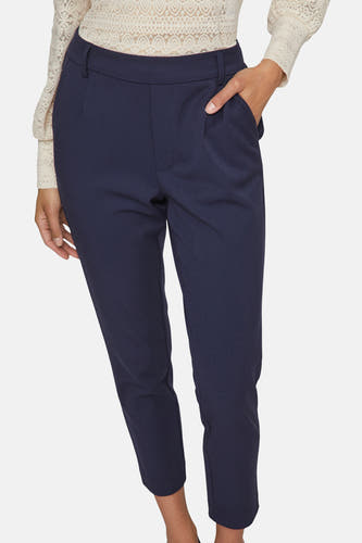 Pantalon bleu de VILA®, avec une main dans la poche et une chemise en dentelle.