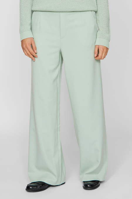 Groene broek van VILA, met wijde pijpen en gedragen met zwarte schoenen.
