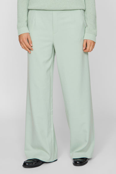 Groene broek van VILA, met wijde pijpen en gedragen met zwarte schoenen.
