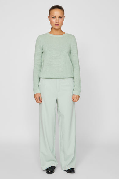 Groene broek van VILA, gecombineerd met een groene trui en zwarte schoenen, staand gepresenteerd tegen een neutrale achtergrond.
