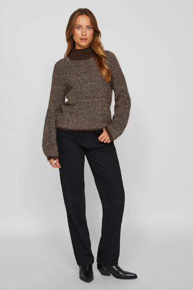 Pull marron avec col montant de VILA®, doté d'un motif à carreaux et de longues manches, associé à des jeans noirs et des bottes en cuir.