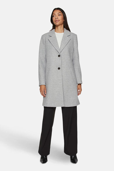Grijze lange jas van VILA®, met zwarte knopen, gecombineerd met een witte trui en zwarte broek.