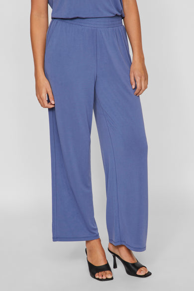 Blauwe broek van VILA, met wijde pijpen en gedragen met zwarte muiltjes met hak.
