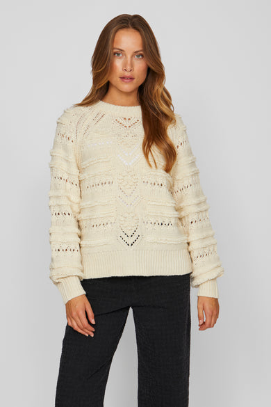 Sweat-shirt écru de VILA, avec un col rond et des détails broés, et des manches longues, porté avec un pantalon noir.