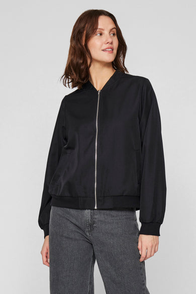 Manteau noir de VILA, avec fermeture à glissière devant, associé à un jean gris.