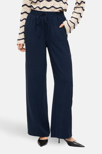 Pantalon bleu de VILA®, avec une taille élastique et des jambes larges, porté avec un pull rayé et des talons noirs.