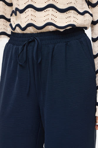 Pantalon bleu de VILA, avec cordon de serrage et texture froissée, combiné avec un pull en maille à motif ondulé.